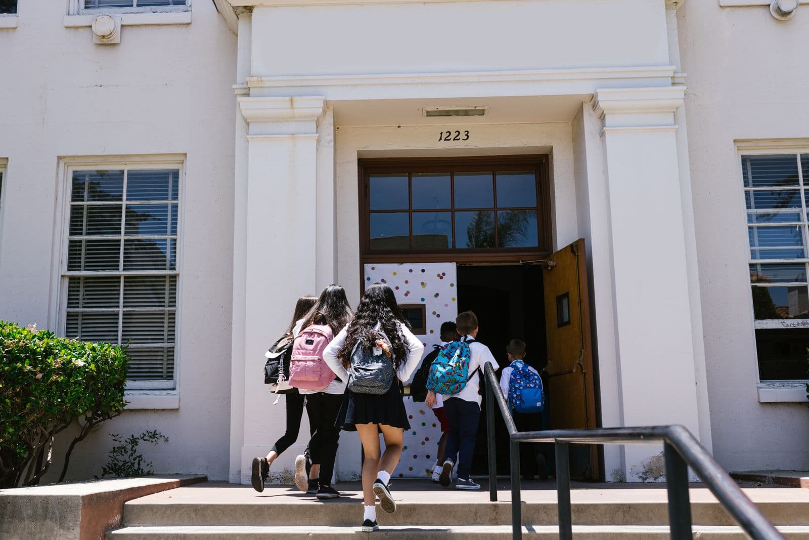 Children with backpacks, seen from behind, walking up the steps into a school