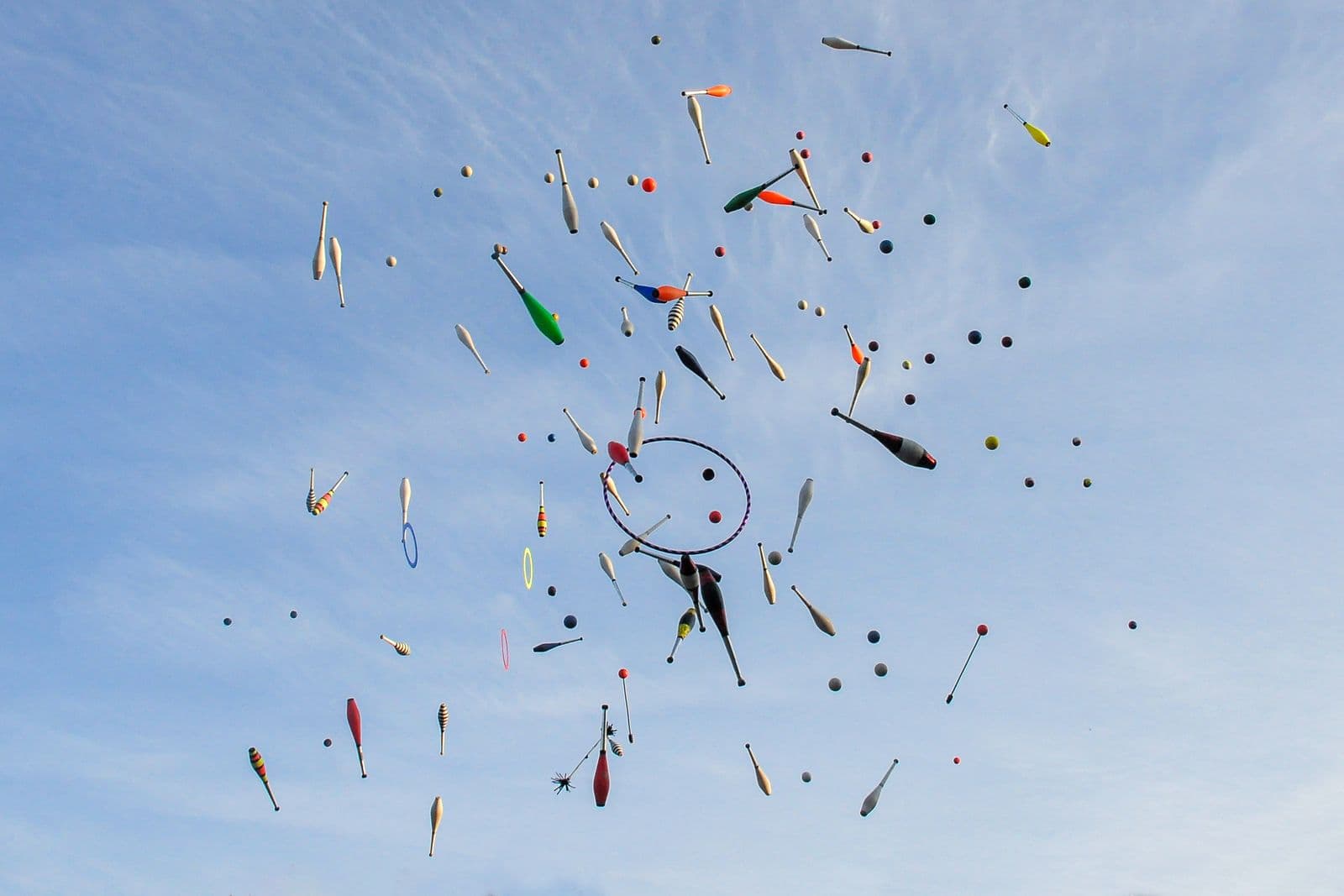 Juggling clubs and rings tossed high against a clear blue sky