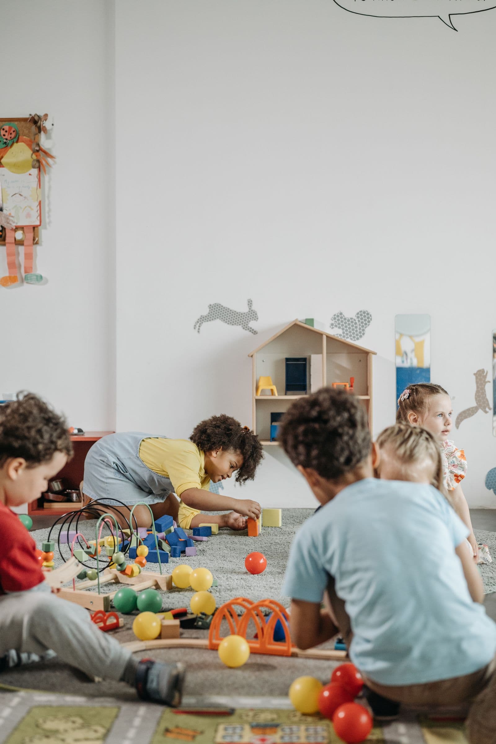 Young children, mostly seen from behind, playing with toys on a daycare playroom floor