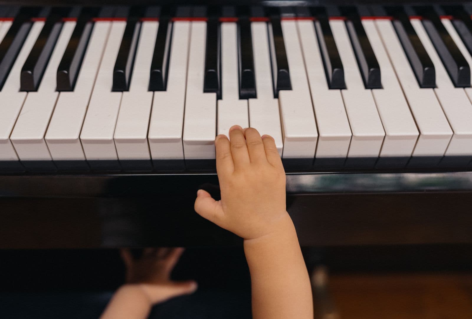 A small child's hand reaching for the keys of a piano