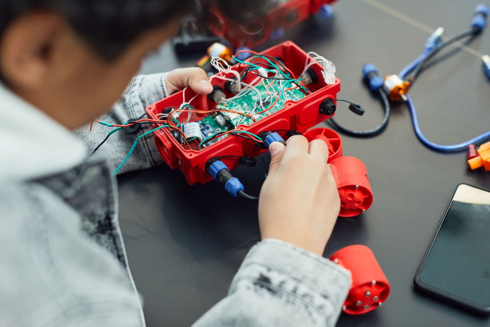 A child's hands wiring a small robot kit on a classroom table