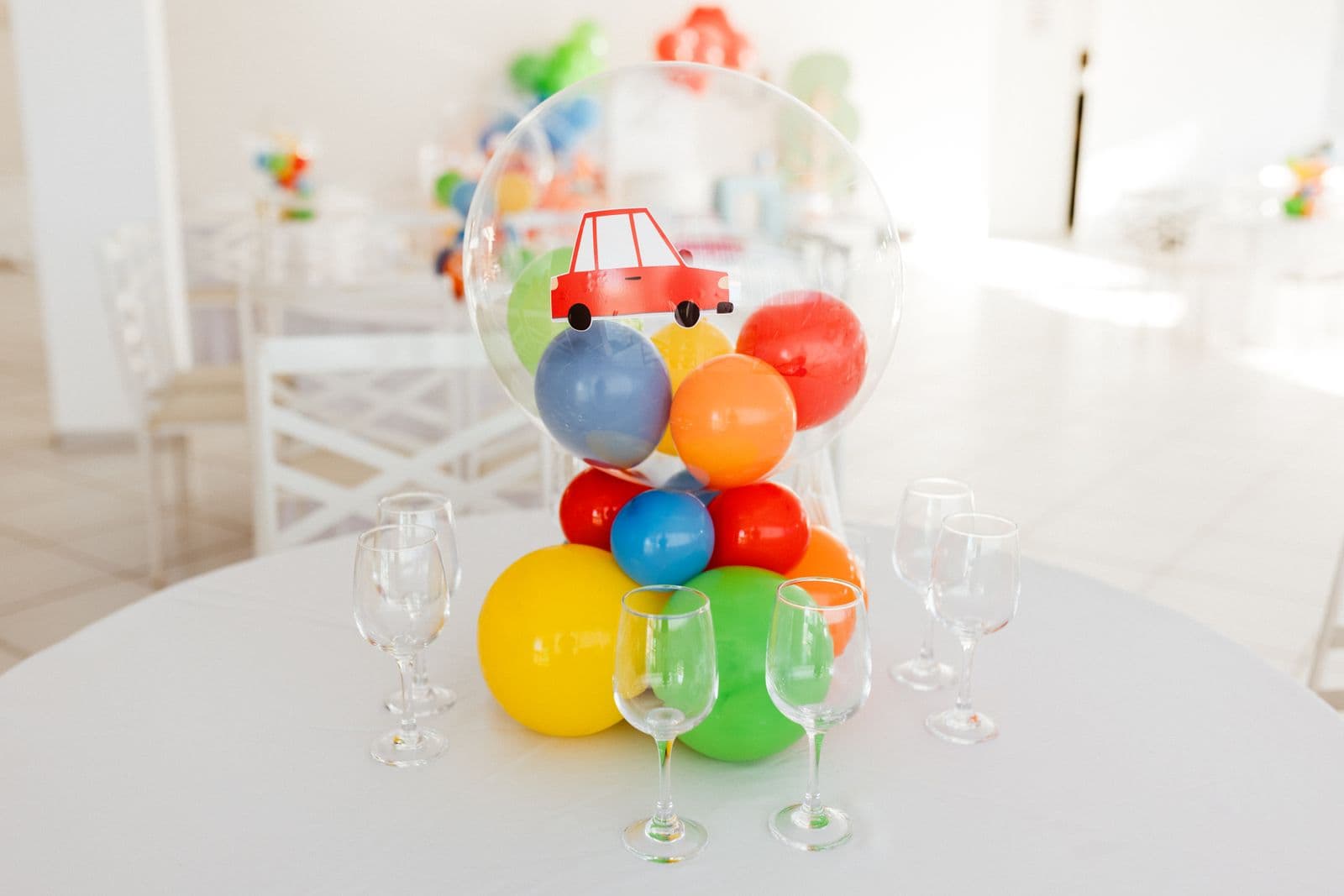 A colourful balloon centrepiece and glasses on a white party table
