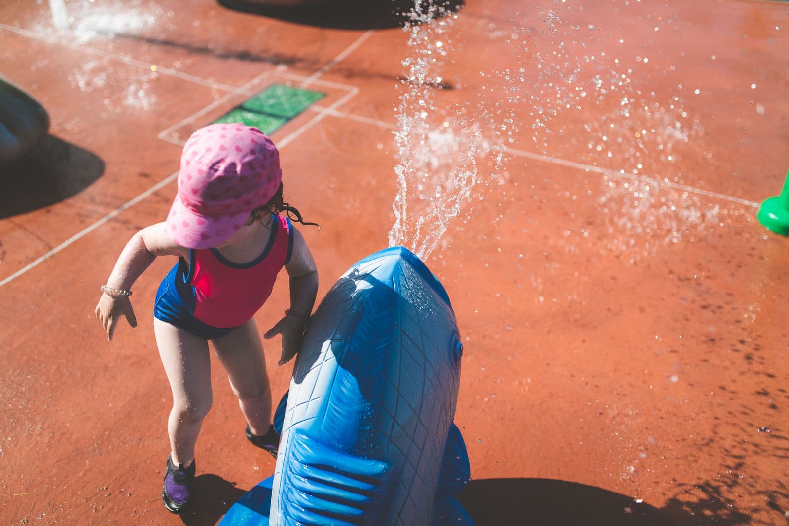 A toddler in a sun hat playing beside a water jet at a splash pad