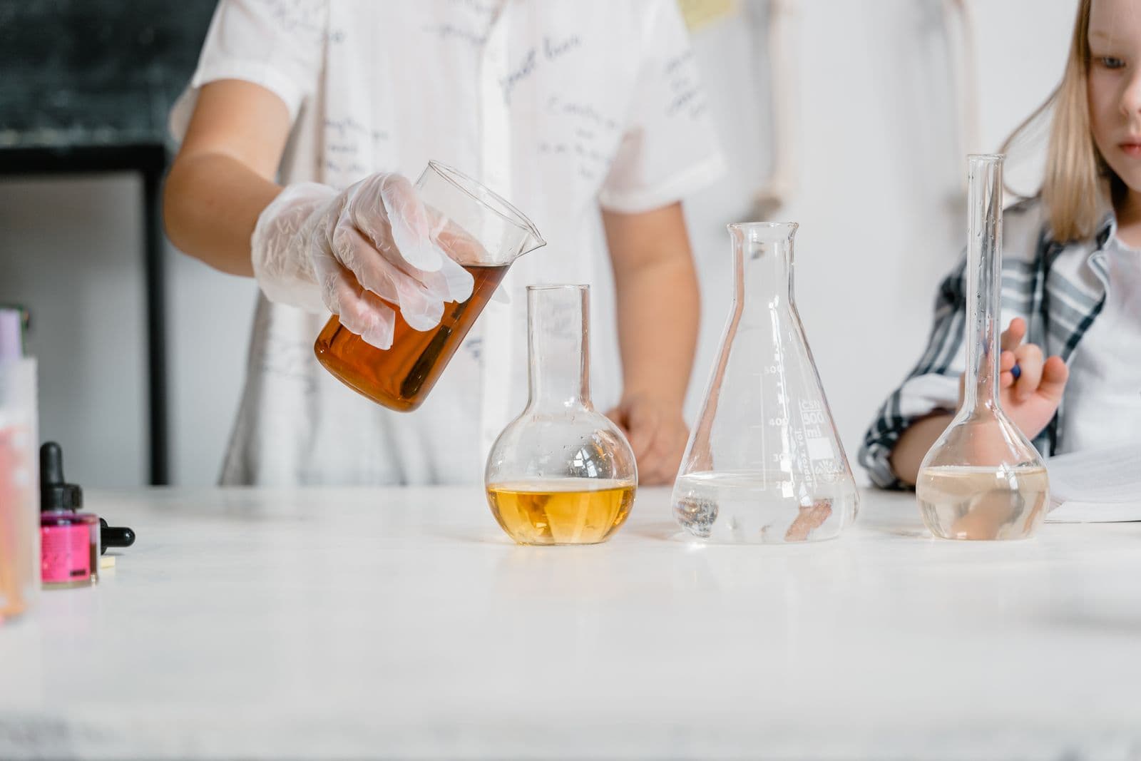 Children's hands pouring coloured liquid between flasks in a science class
