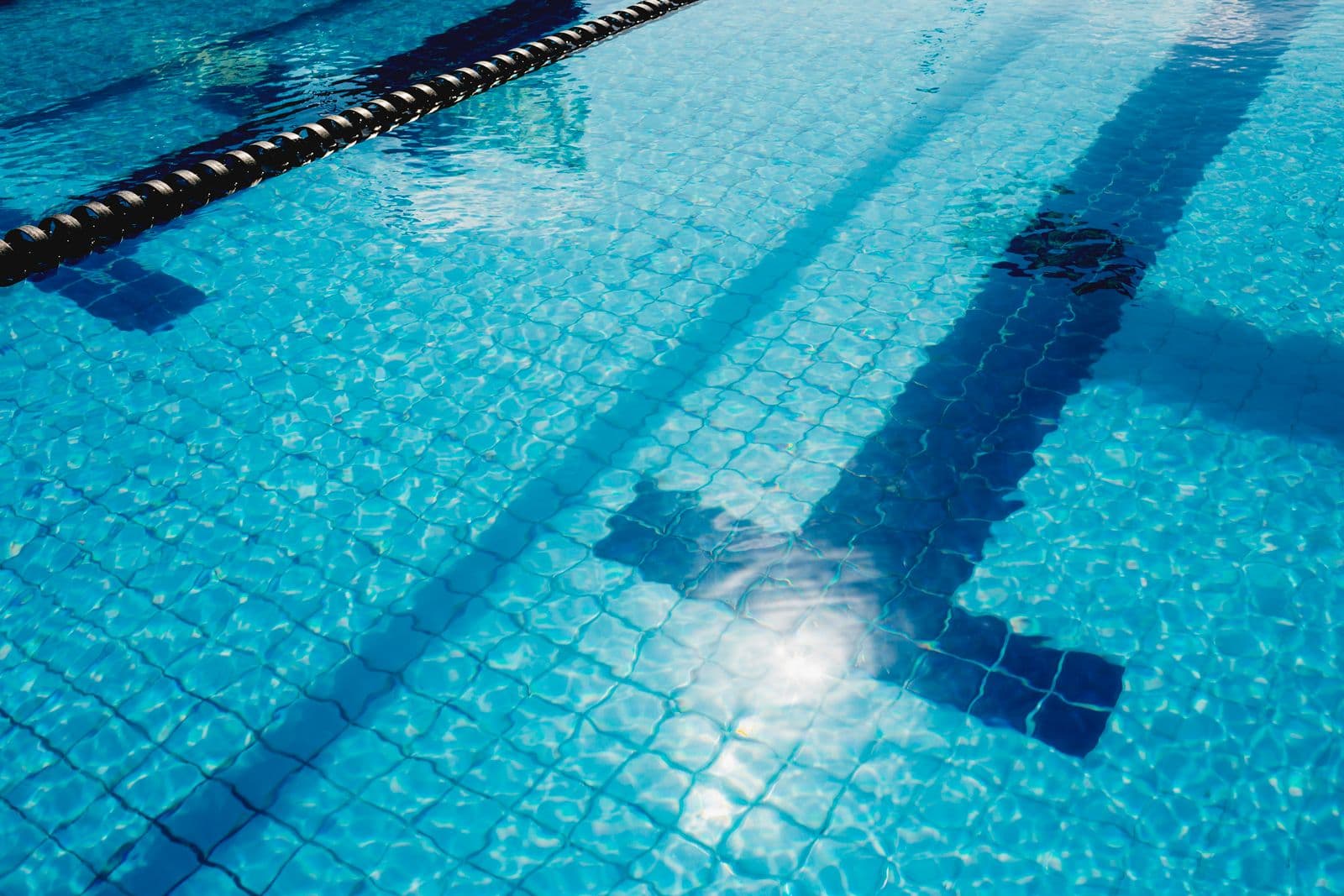 Sunlit swimming pool with clear water, tiled lane markings and a lane rope