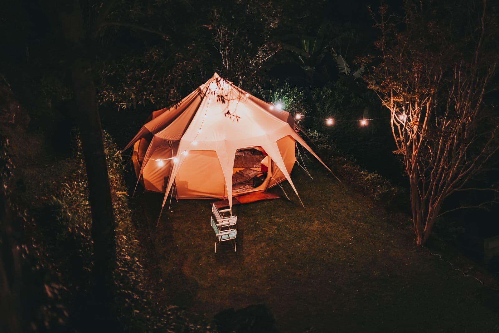 A glowing bell tent with string lights on a lawn at night